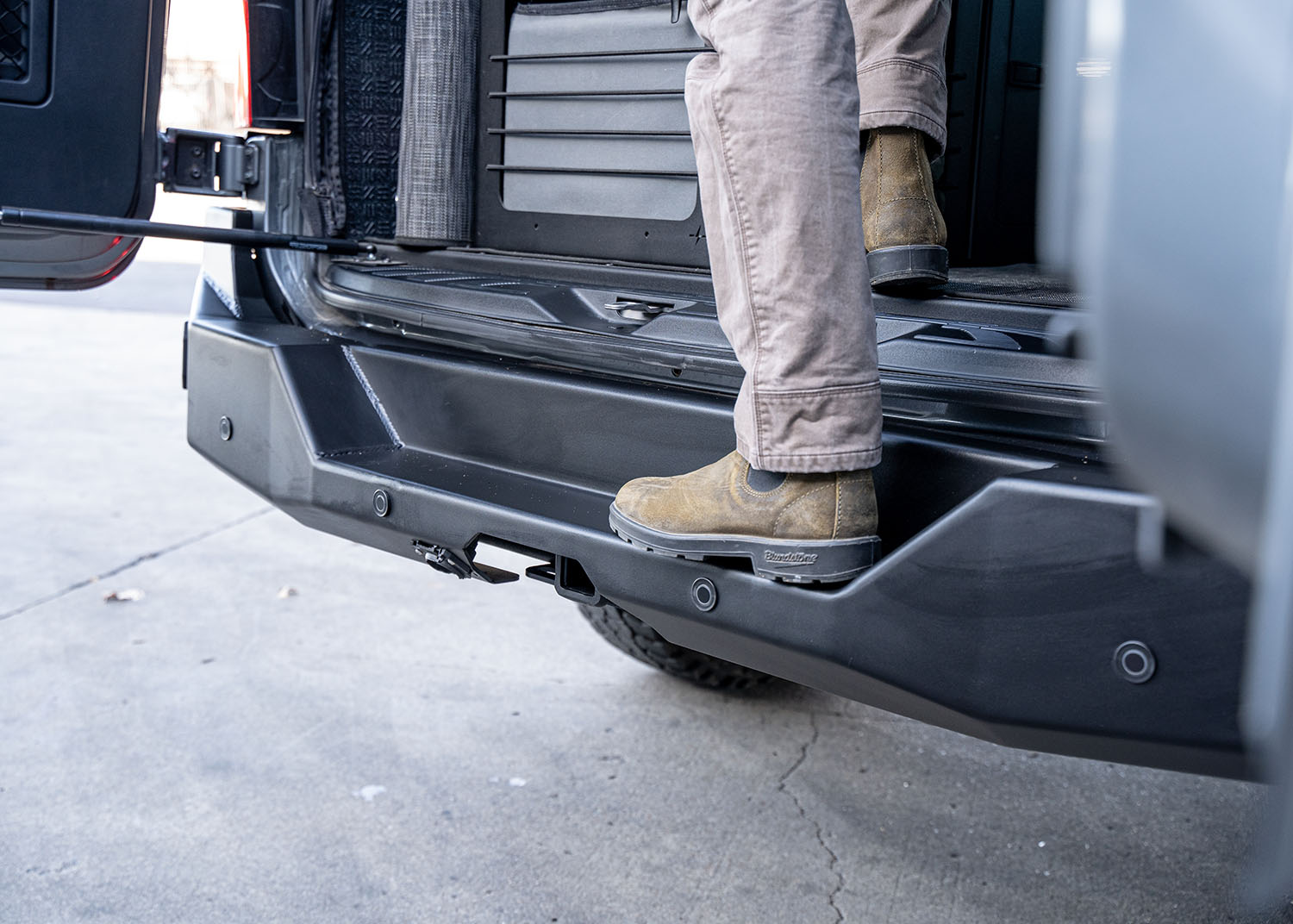 Close-up shot of the rear step on the ROAMBUILT Rear Bumper for the Mercedes Sprinter van, highlighting the sturdy aluminum construction, textured black powder coat finish, and integrated design for easy access to the rear cargo area.