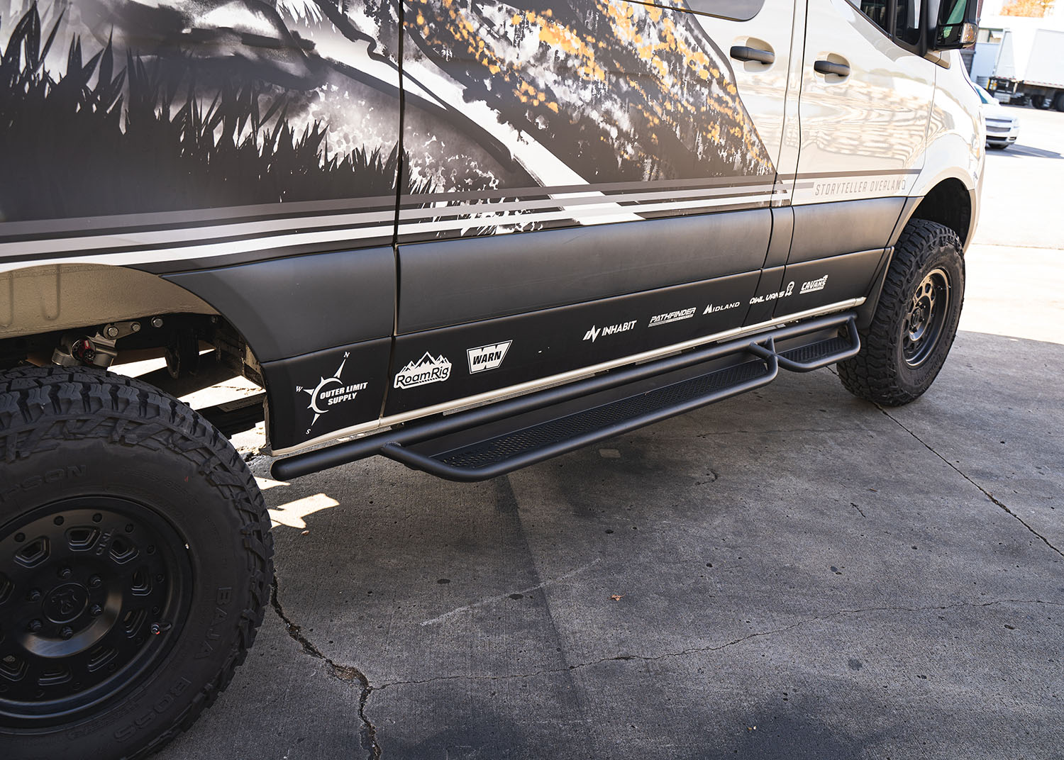Rear-side view of ROAMBUILT Passenger Side Tube Step on Mercedes Sprinter, showing tubular design and perforated traction decking from the back angle.