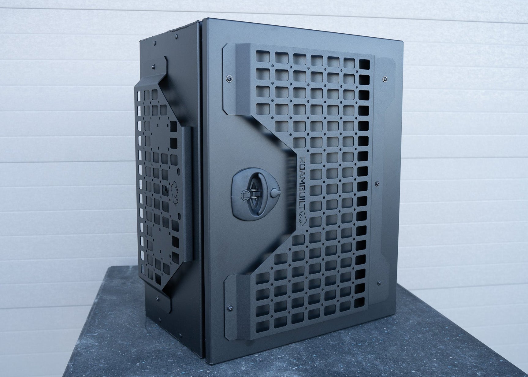 Front and angled side view of ROAMBUILT Universal Aluminum Storage Box showing MOLLE panels on the front and side, with visible black compression latch.