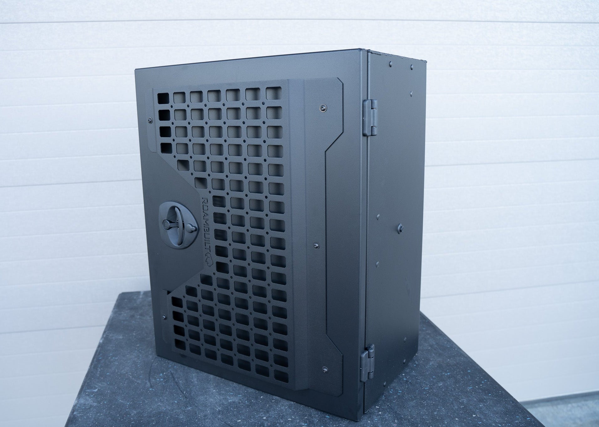 Angled view of the Universal Aluminum Storage Box highlighting the front MOLLE panel and black lockable compression latch, showcasing its rugged design, accessory mounting capability, and secure closure system.