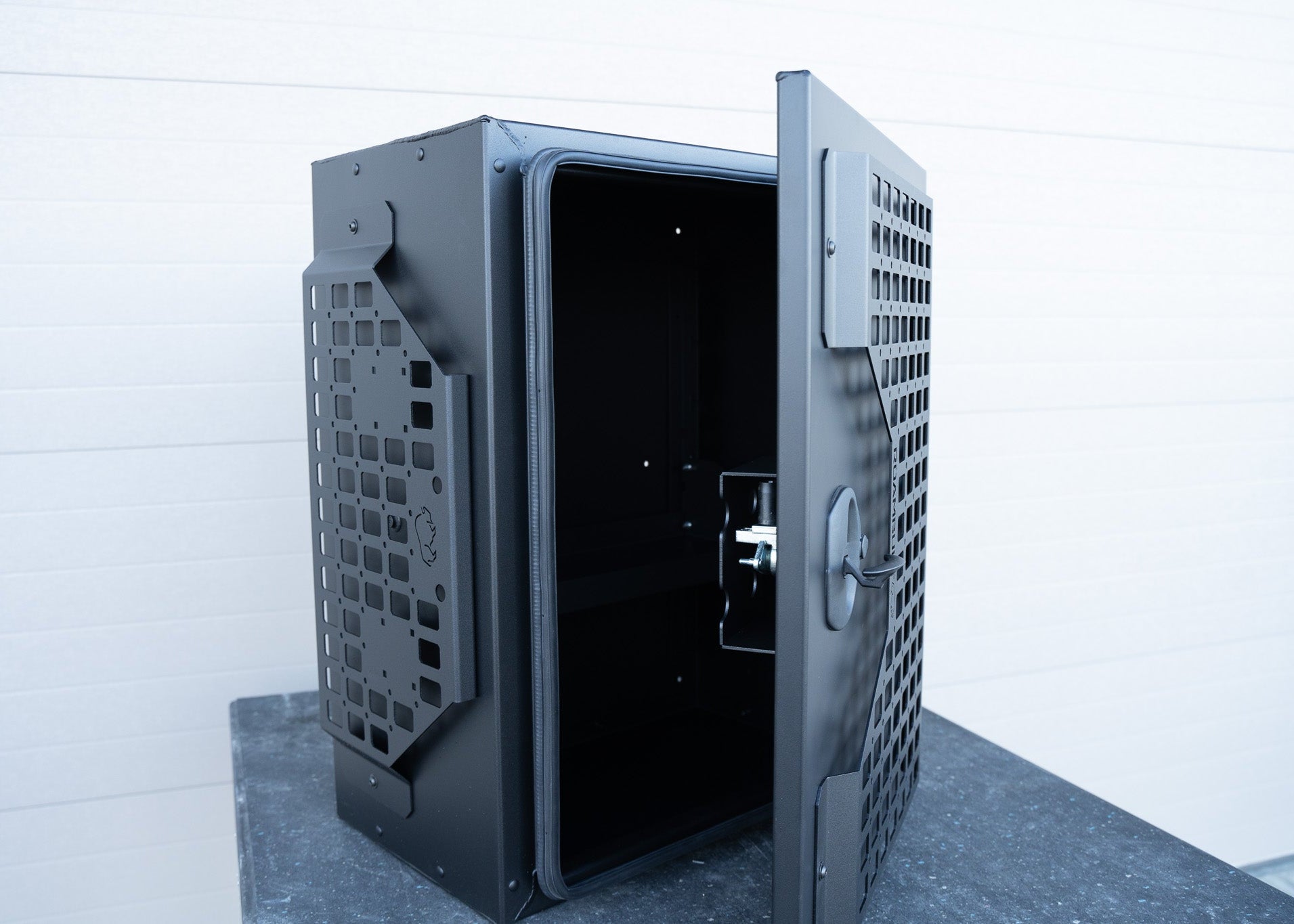 Door of ROAMBUILT Universal Aluminum Storage Box half open, revealing both sides of the black lockable compression latch, exterior molle panels, and the water-resistant gasket lining.