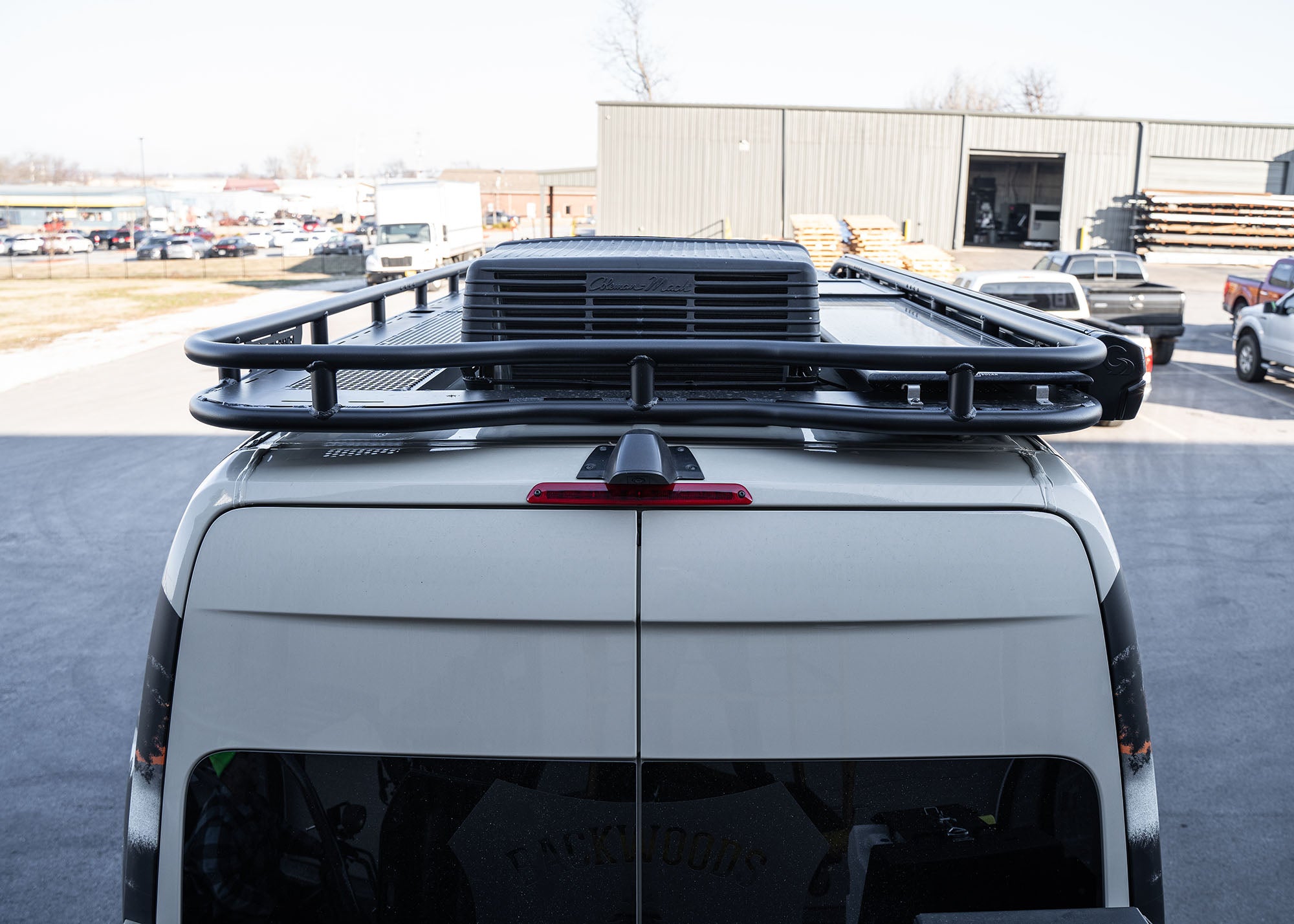 Eye-level close-up of the rear portion of the ROAMBUILT Safari 2.0 roof rack, showing the A/C unit cutout, curved rear design for rear camera clearance, and mounted solar panel.