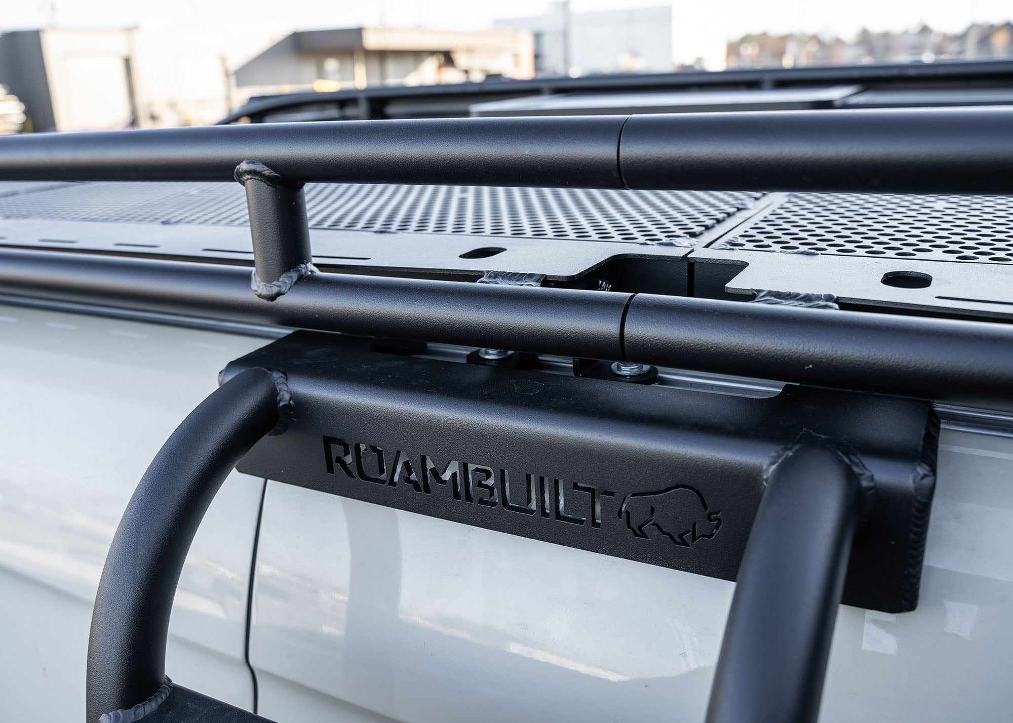 Close-up of the ROAMBUILT Chicane ladder mounted securely beneath the Safari 2.0 roof rack, directly attached to the factory roof railing for a strong, flush fit.