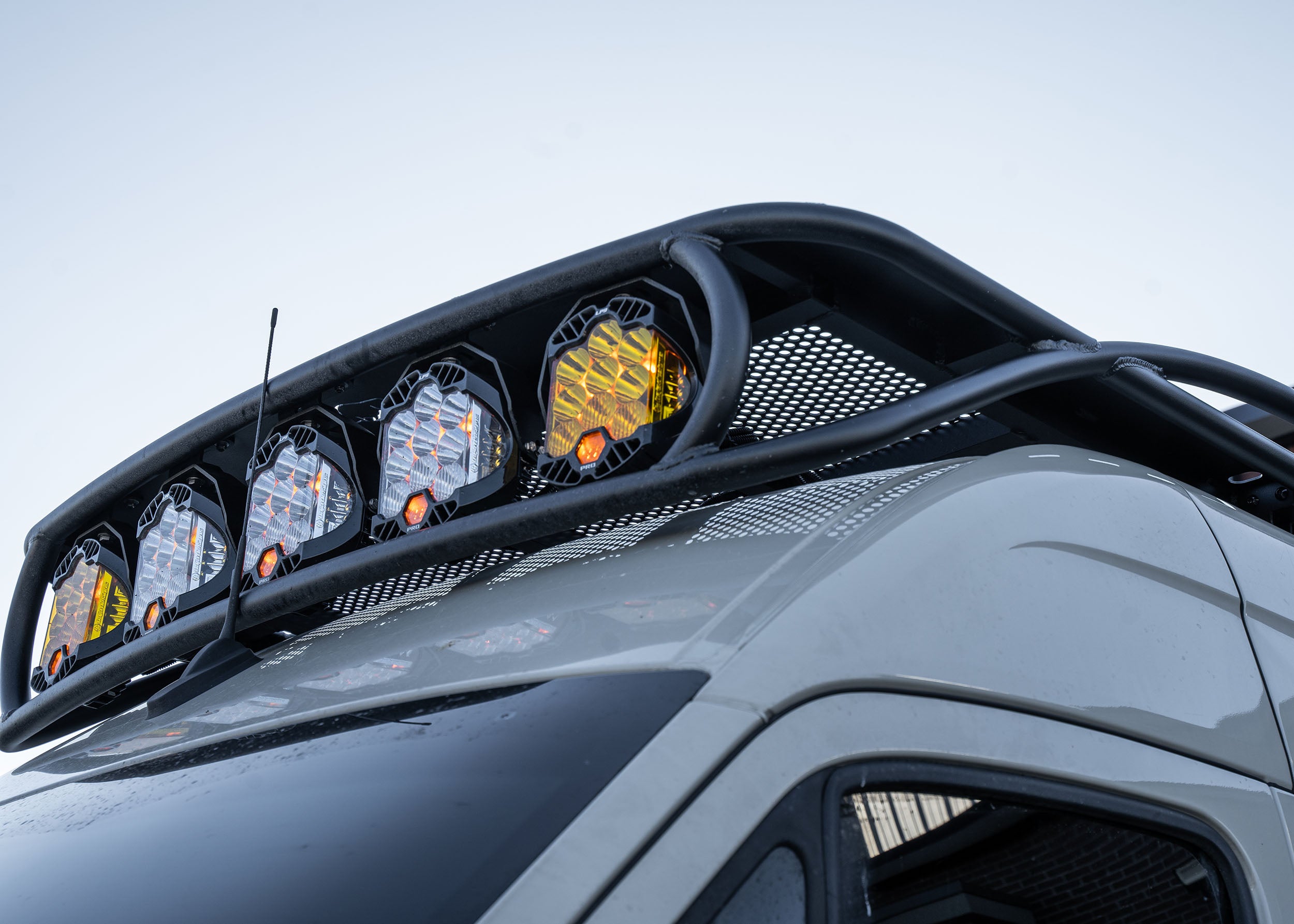 Close-up upward view from the driver side showing the front curvature of the Safari 2.0 roof rack, with mounted Baja Designs lights and aerodynamic contour.