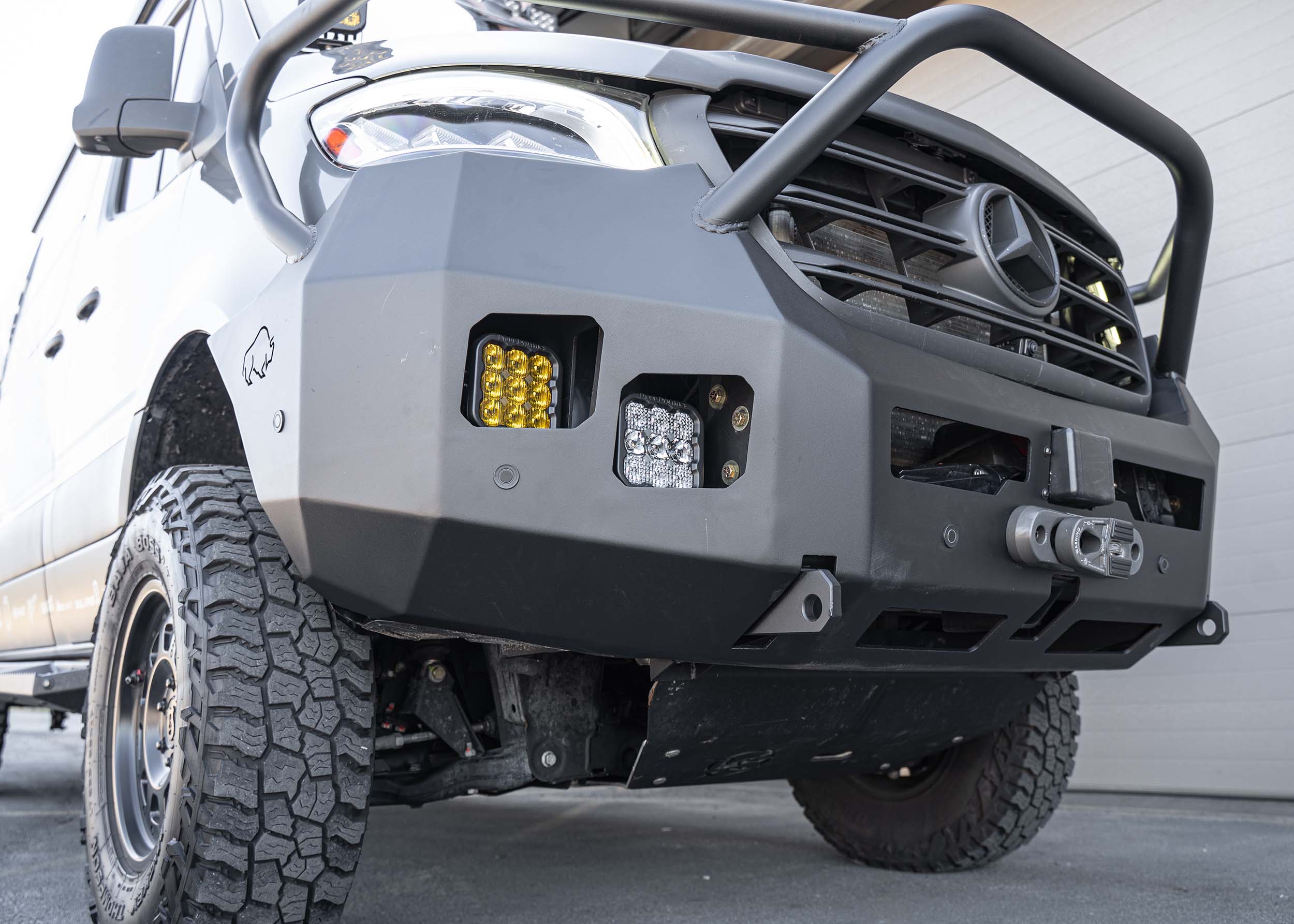 Bottom-up view from the passenger side of ROAMBUILT Full Guard Front Bumper on a Mercedes Sprinter, highlighting underside structure and wrap-around protection.