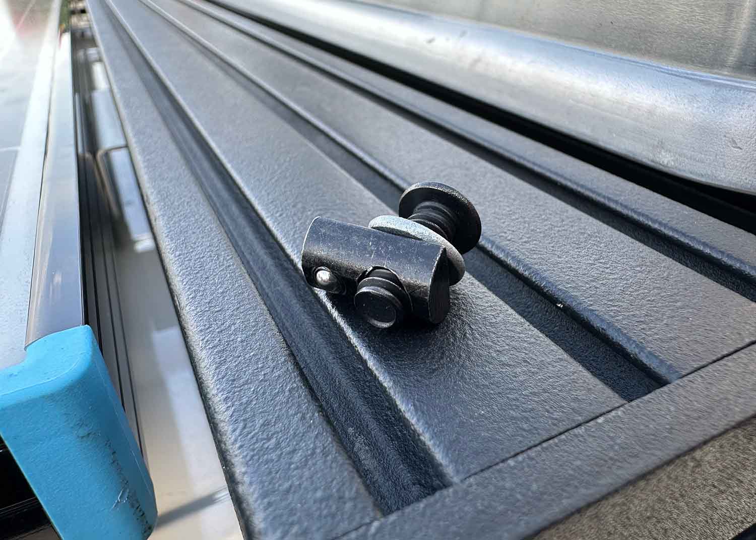 Close-up of assembled mounting hardware showing black oxide bolt threaded through lock washer into a slide-in T-nut, ready for installation on ROAMBUILT Flatpack Roof Rack.
