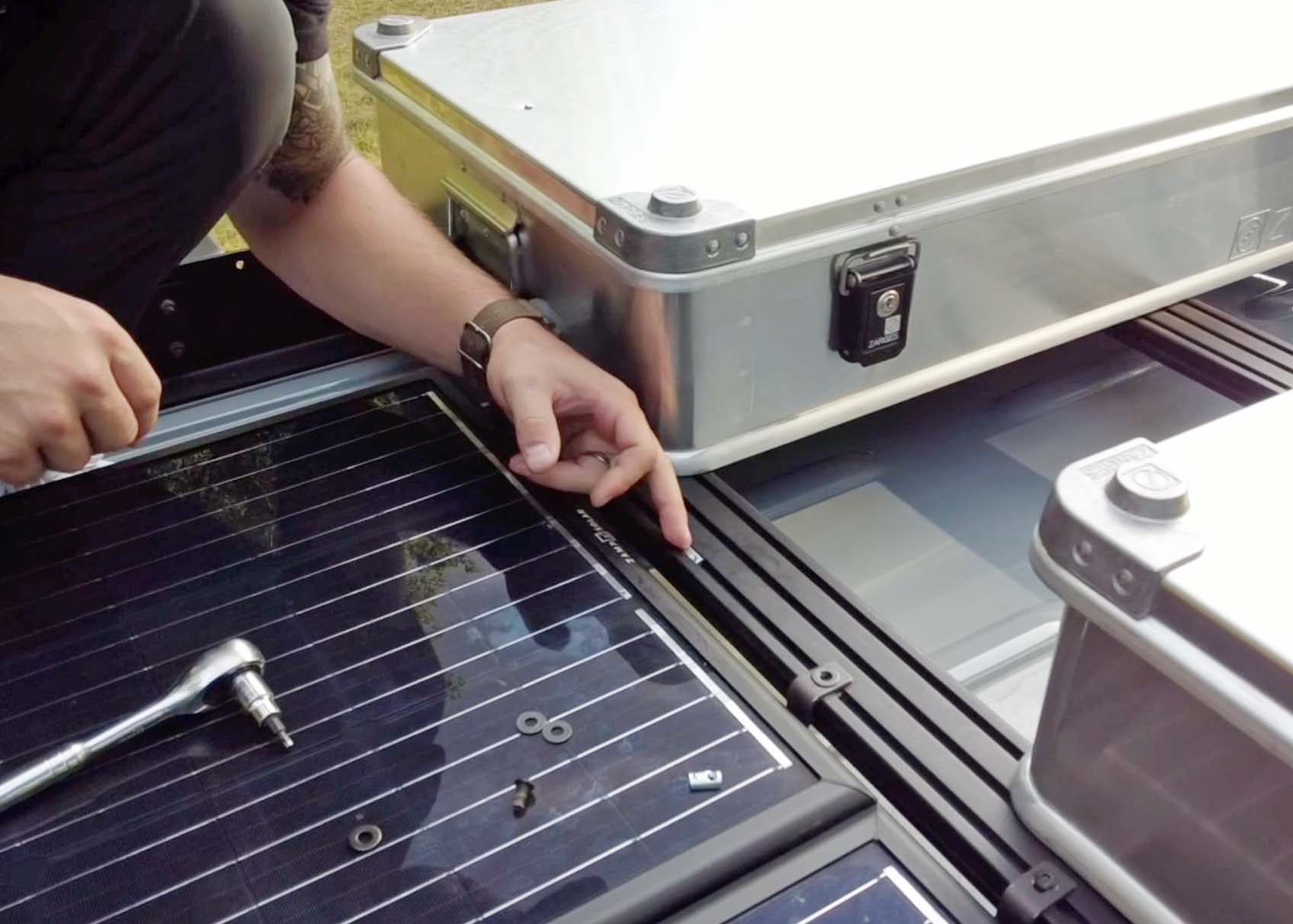 Close-up view of solar panel and gear being securely mounted to ROAMBUILT Flatpack Roof Rack using black oxide slide-in T-nuts, lock washers, and screws from the accessory hardware kit.
