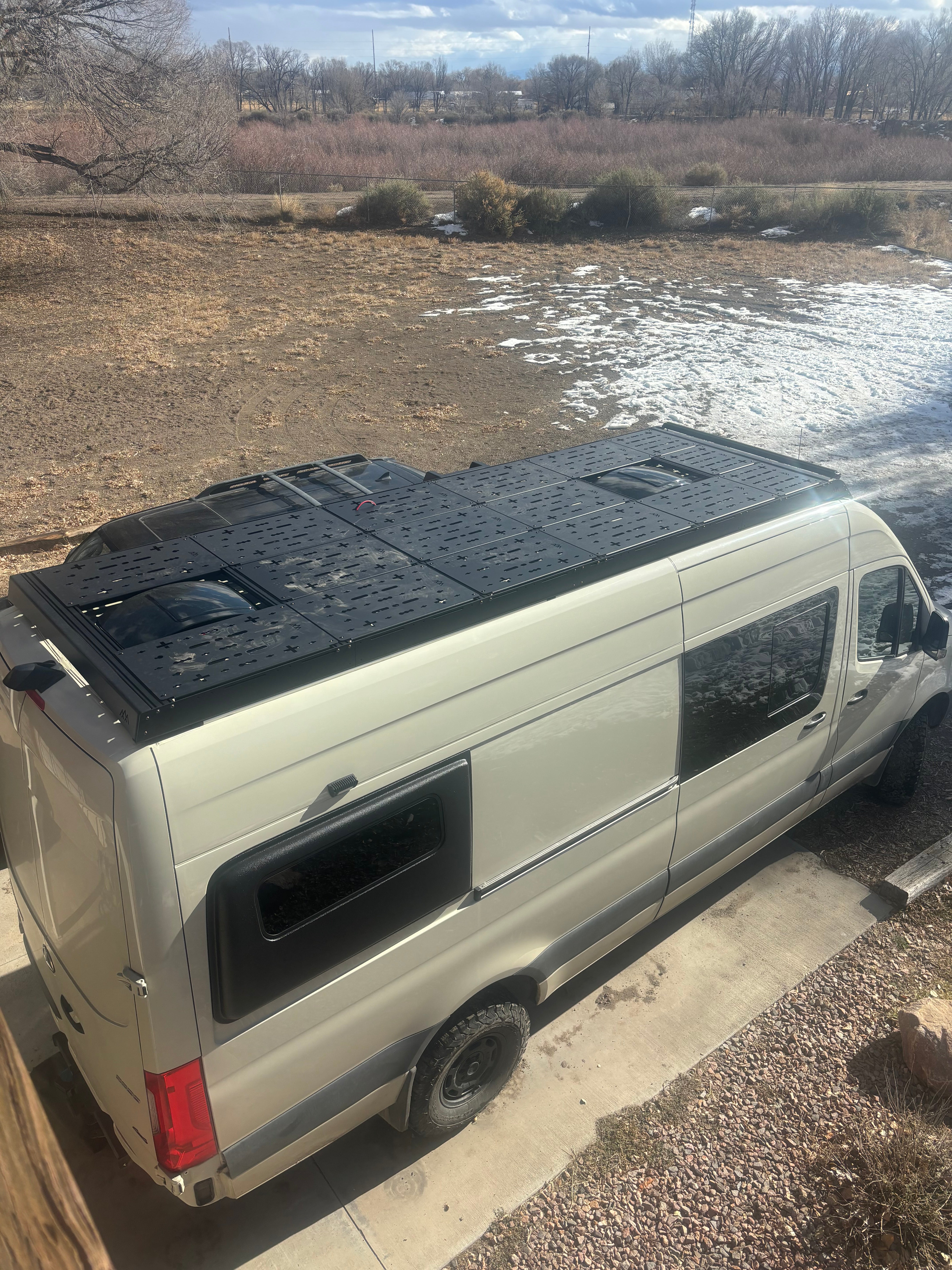 Drone view of entire van roof equipped with ROAMBUILT deck panels, set up for storage and lounging, showcasing full rooftop utility and layout.