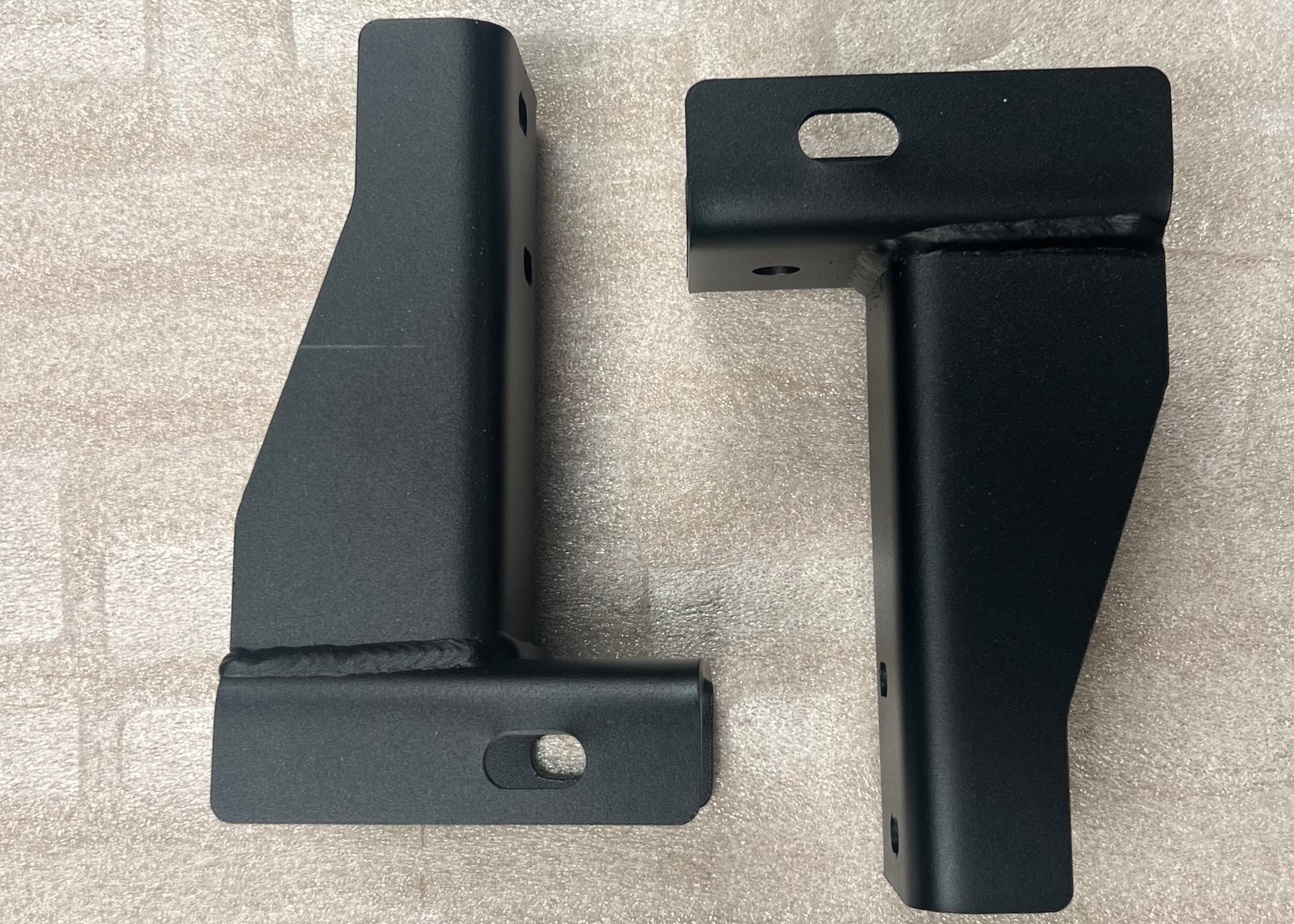 Top-side angled view of a pair of ROAMBUILT replacement frame brackets for 2019+ Mercedes Sprinter 2WD and 3500 dually models, showing custom-fabricated steel construction and mounting points.